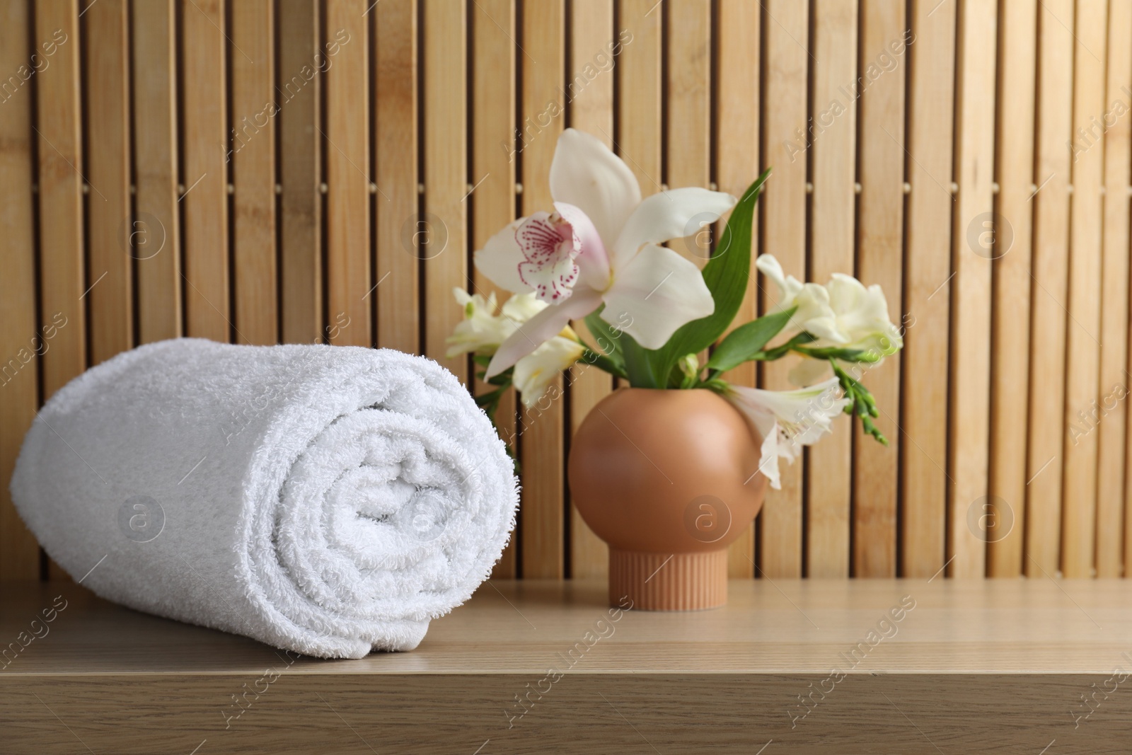 Photo of Rolled terry towel and beautiful flowers on wooden table