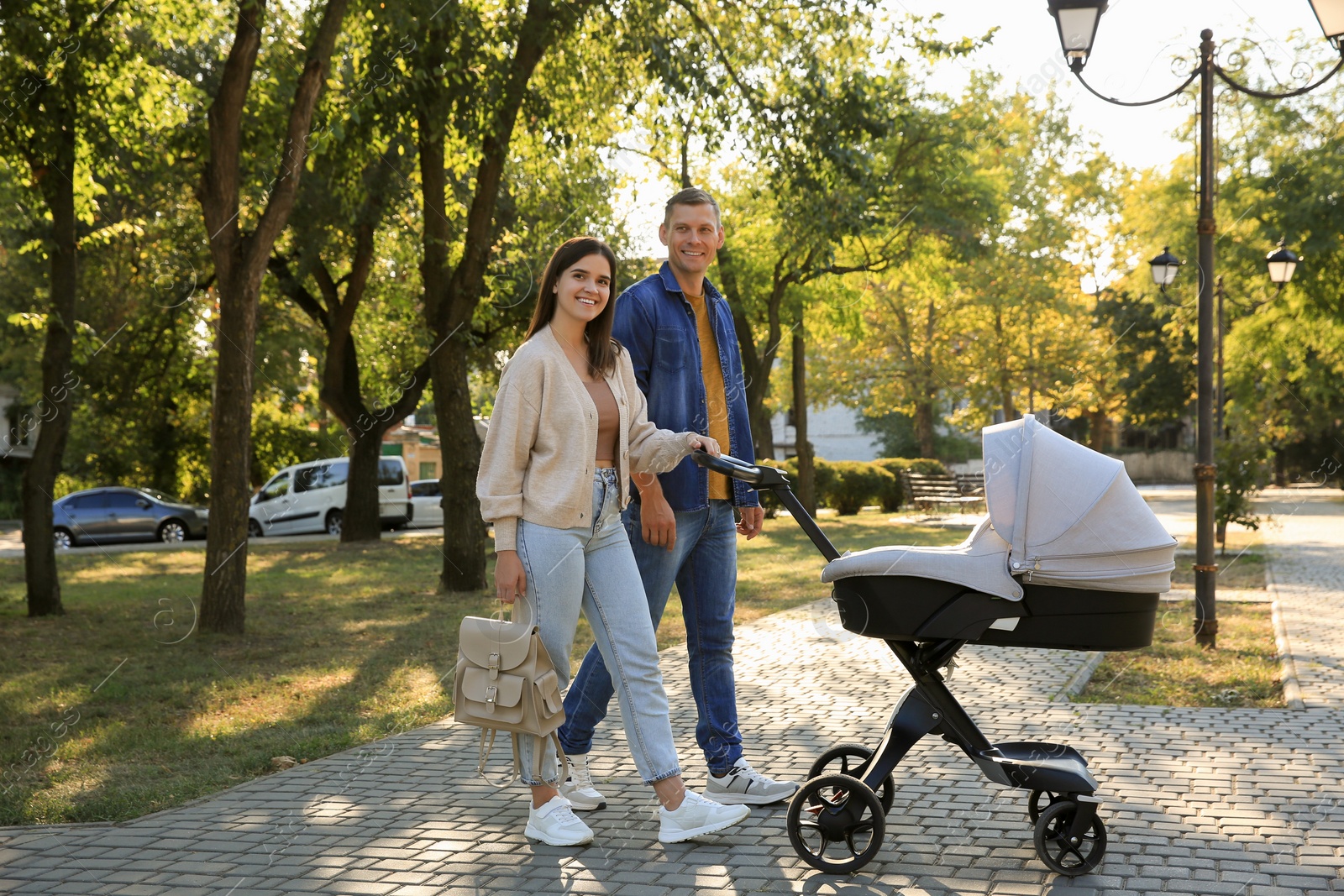 Photo of Happy parents walking with their baby in stroller at park on sunny day