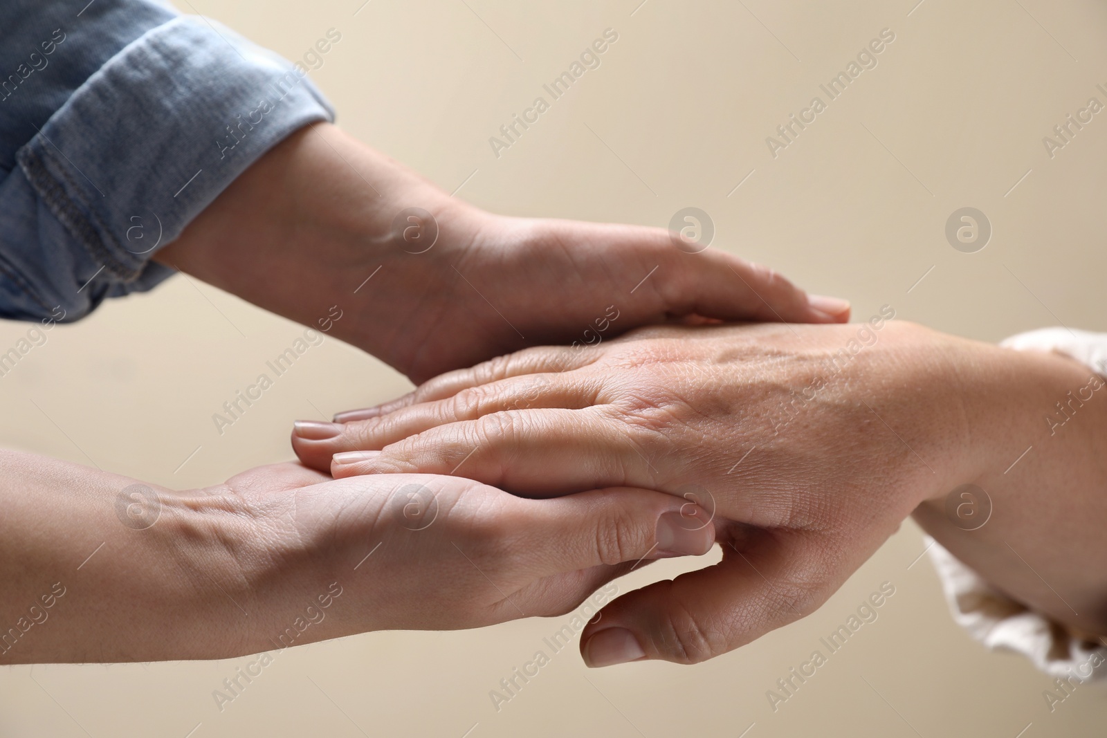 Photo of Woman holding hands with her mother on beige background, closeup