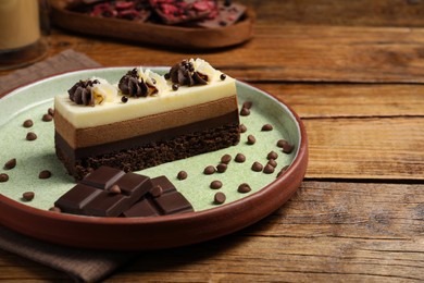 Photo of Plate with tasty mousse cake and chocolate on wooden table, space for text