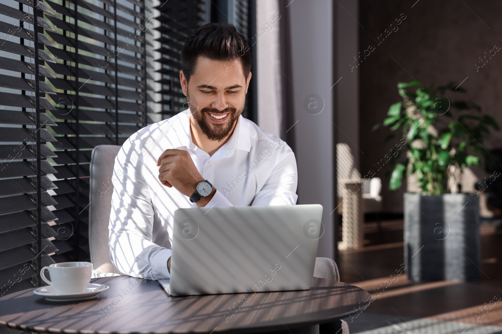 Photo of Happy young man working on laptop at table in office. Space for text