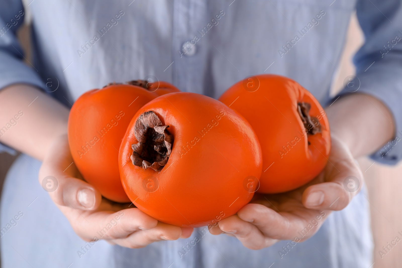 Photo of Woman holding delicious ripe juicy persimmons on blurred background, closeup