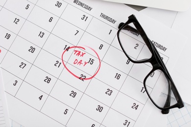 Photo of Calendar page with date reminder and glasses, top view. Tax day