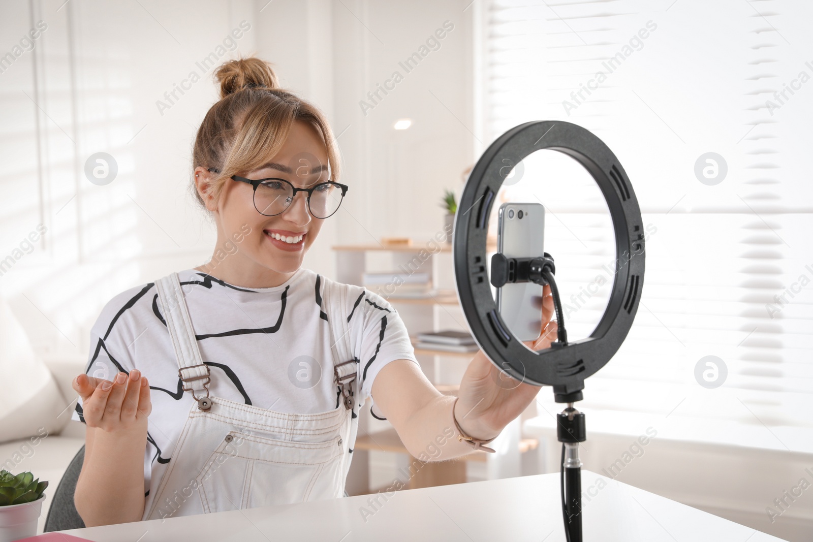 Photo of Blogger recording video at table in room. Using ring lamp and smartphone