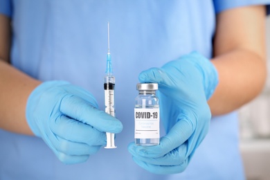 Doctor with coronavirus vaccine and syringe in laboratory, closeup