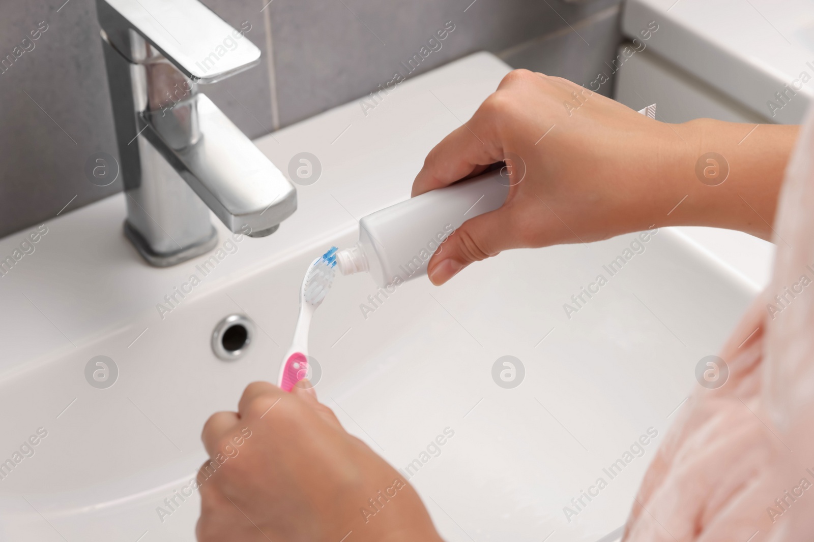 Photo of Woman applying toothpaste on brush in bathroom, closeup