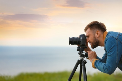 Photo of Male photographer taking picture of beautiful landscape with professional camera outdoors. Space for text