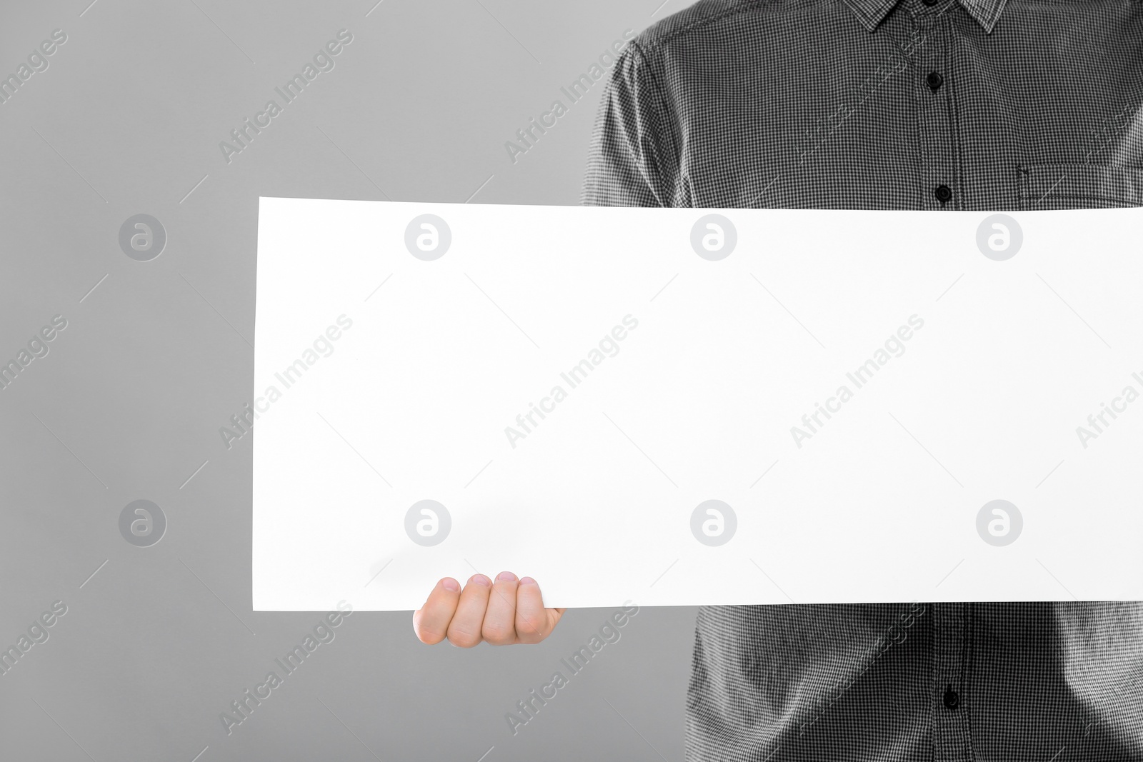 Photo of Man holding sheet of paper on grey background, closeup. Mockup for design