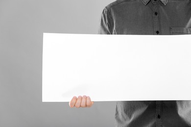Man holding sheet of paper on grey background, closeup. Mockup for design