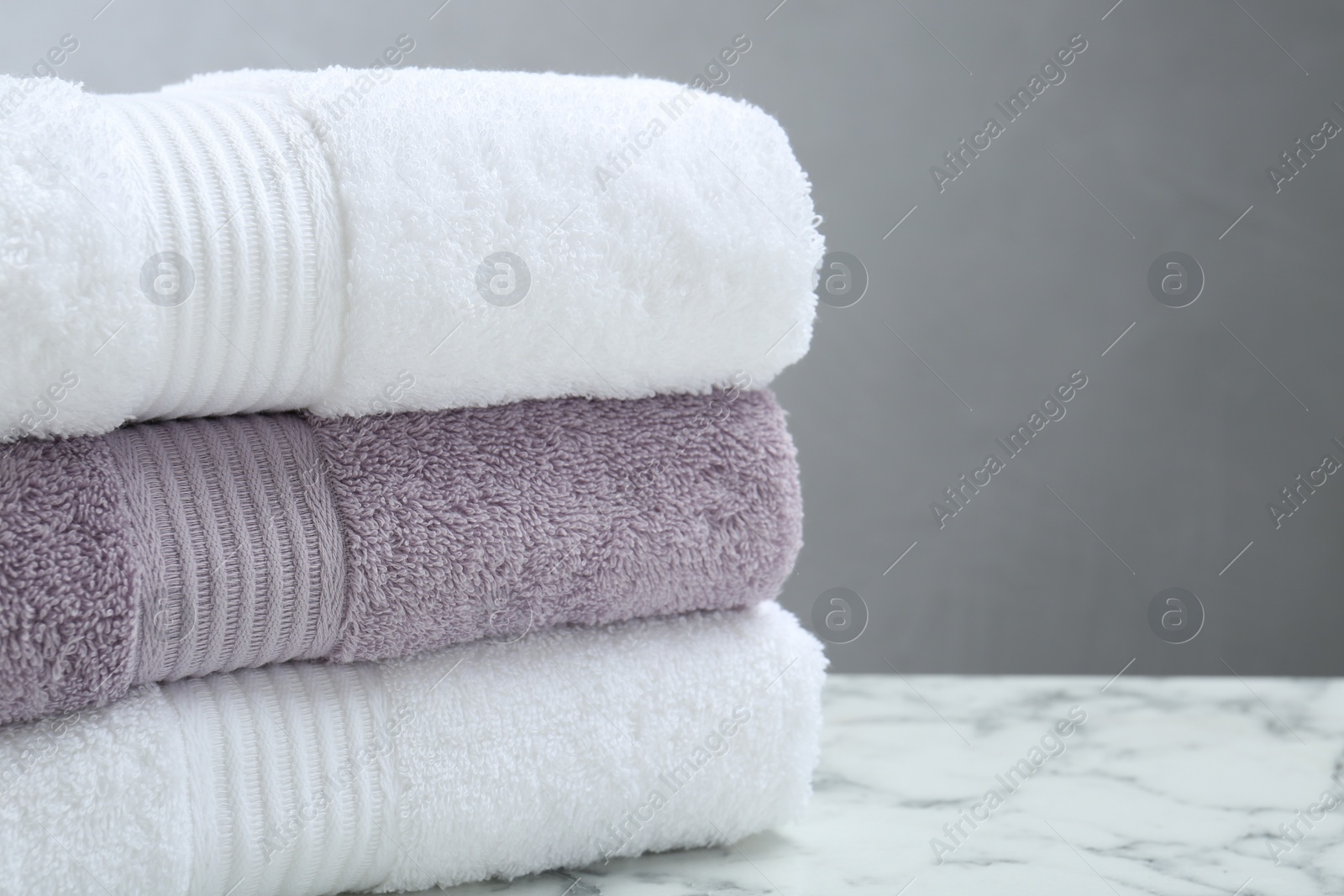 Photo of Stack of folded terry towels on white marble table, closeup. Space for text