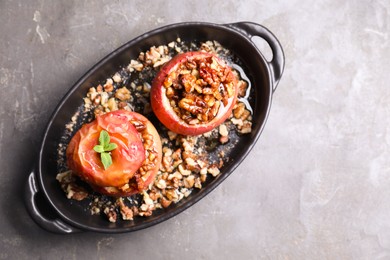 Photo of Tasty baked apples with nuts, honey and mint in baking dish on gray textured table, top view. Space for text