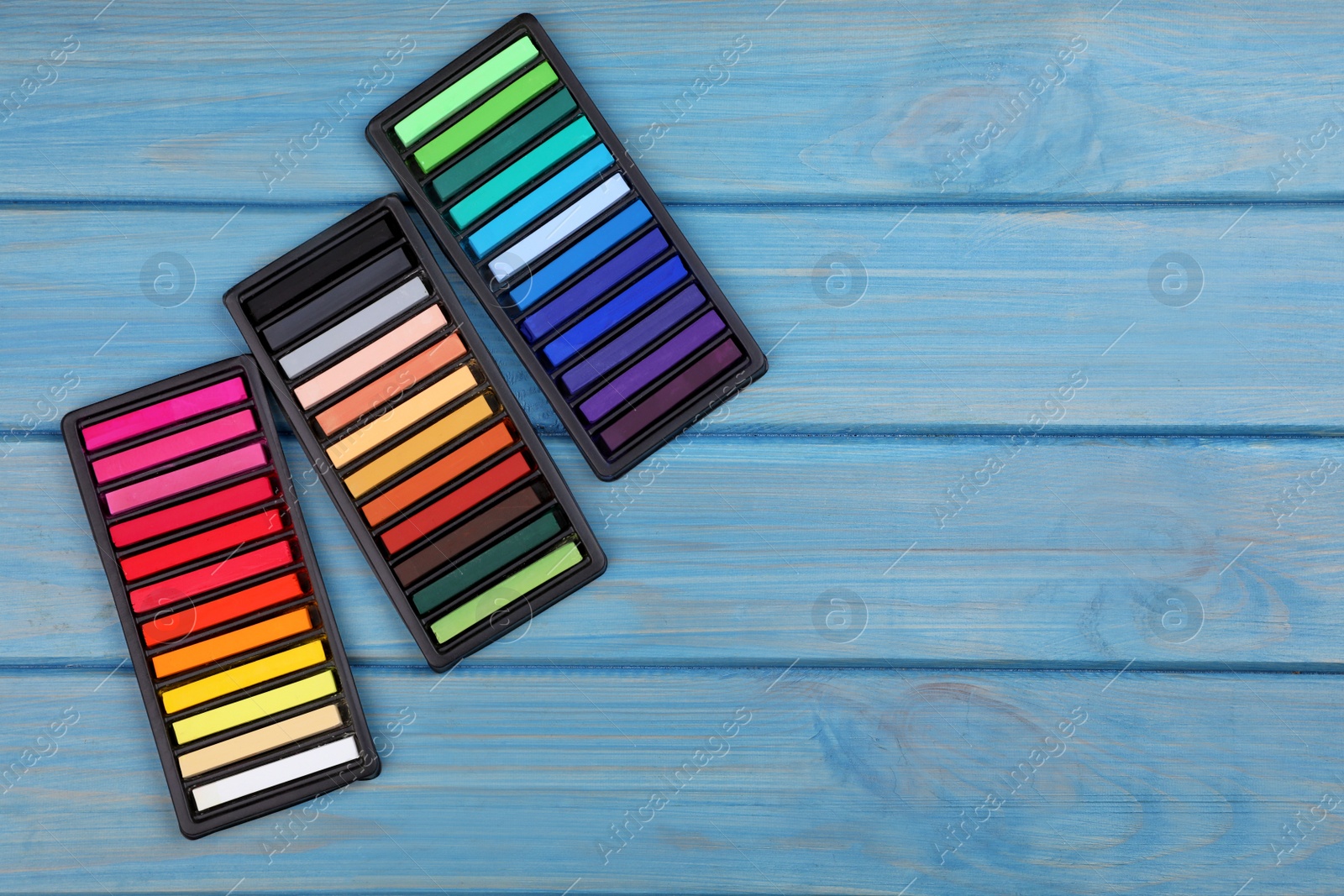 Photo of Colorful pastels in trays on light blue wooden table, flat lay with space for text. Drawing materials