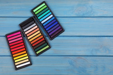 Colorful pastels in trays on light blue wooden table, flat lay with space for text. Drawing materials