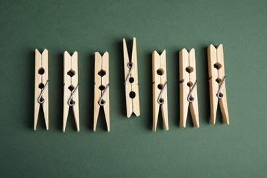 Wooden clothespins on dark green background, flat lay