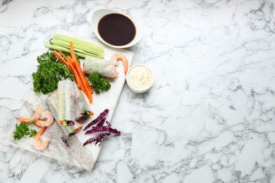 Photo of Delicious rolls wrapped in rice paper served on marble table, flat lay. Space for text