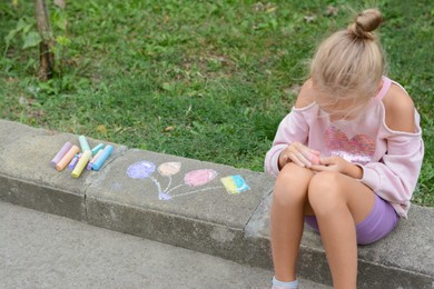 Little child chalk piece sitting on curb outdoors, space for text