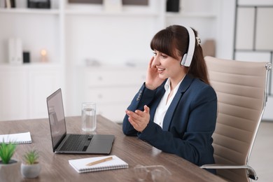 Photo of Woman in headphones using video chat during webinar at wooden table in office