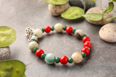 Photo of Beautiful bracelet with gemstones, leaves and stones on grey background, closeup