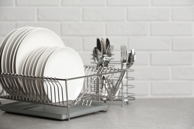 Dish rack with clean plates on table near brick wall. Space for text