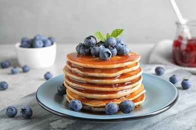 Photo of Plate of delicious pancakes with fresh blueberries and syrup on grey table against light background