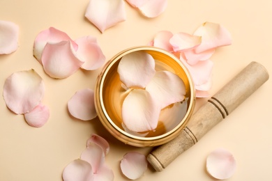 Photo of Golden singing bowl with petals and mallet on beige background, flat lay. Sound healing