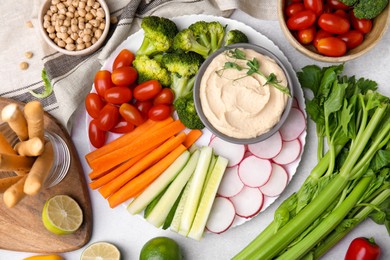 Plate with delicious hummus and fresh vegetables on light grey table, flat lay