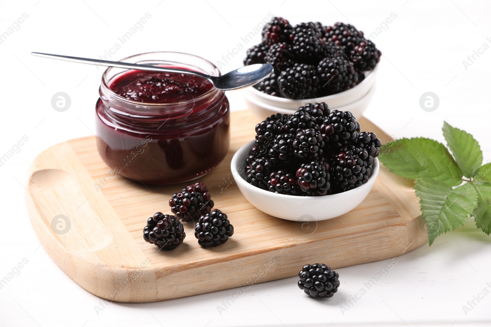 Photo of Fresh ripe blackberries, tasty jam and leaves on white wooden table