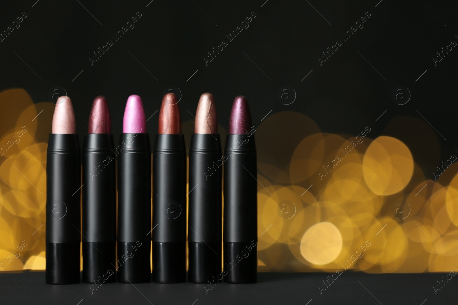 Photo of Set of bright lipsticks on table against blurred lights, space for text