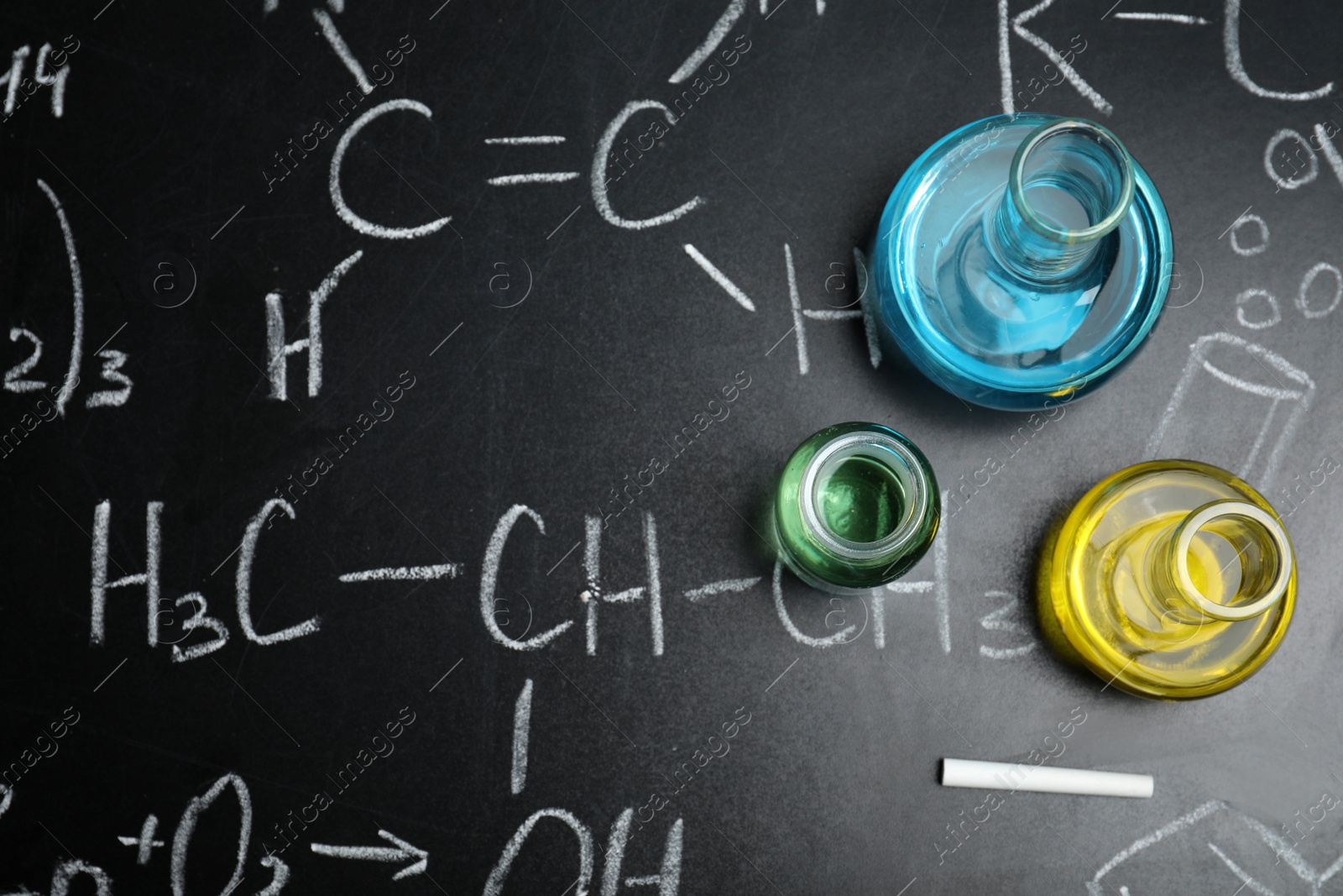 Photo of Laboratory glassware on blackboard with chemical formulas, flat lay