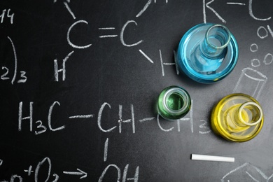 Photo of Laboratory glassware on blackboard with chemical formulas, flat lay