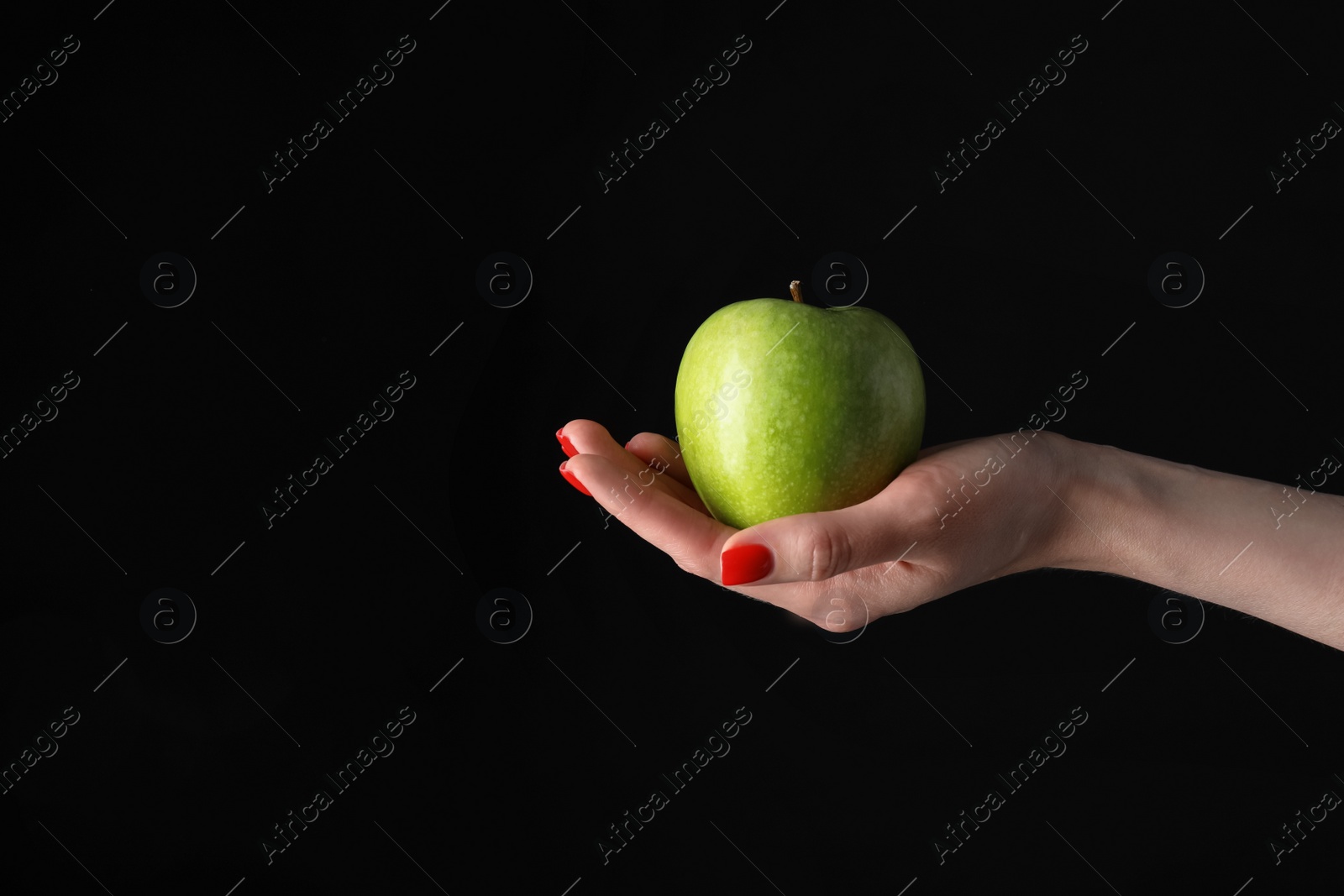 Photo of Woman holding fresh ripe green apple against black background, closeup