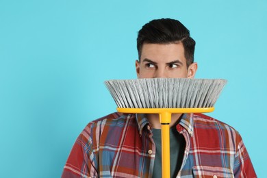 Man with yellow broom on light blue background, space for text