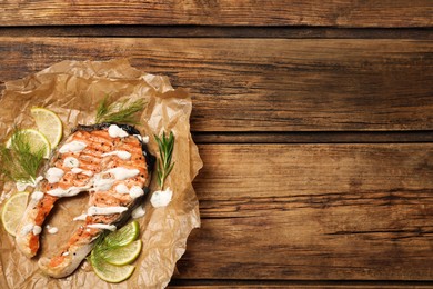 Photo of Tasty salmon steak with sauce, citrus slices and herbs on wooden table, top view. Space for text