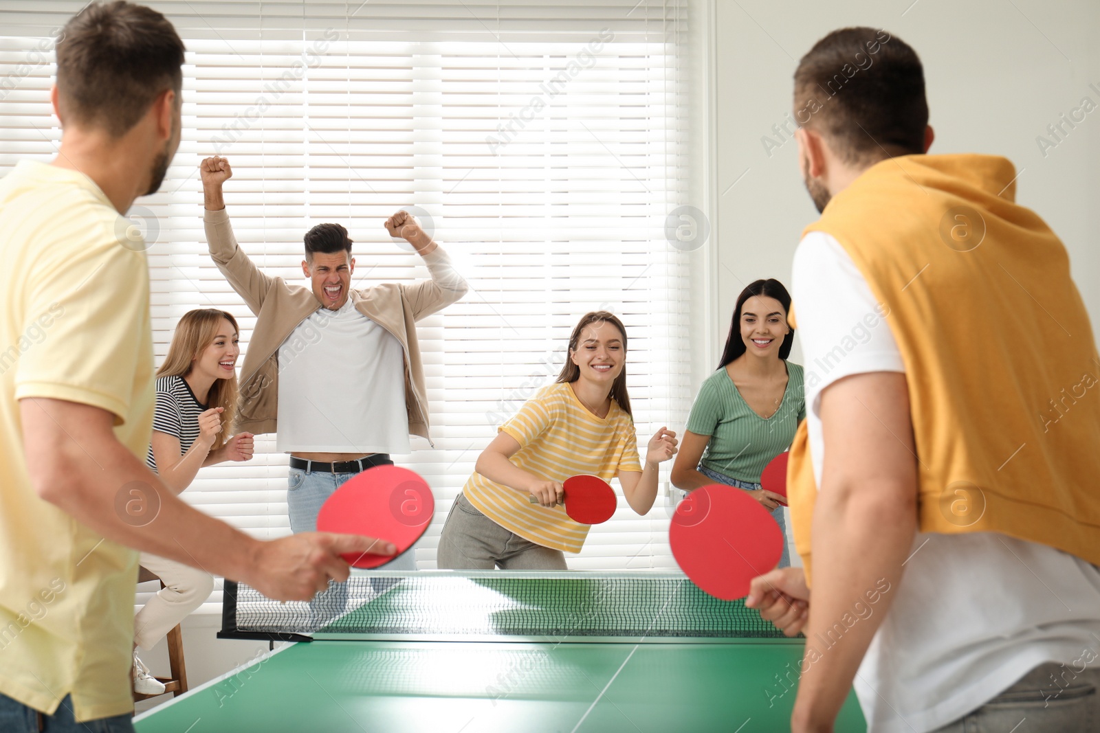 Photo of Happy friends playing ping pong together indoors