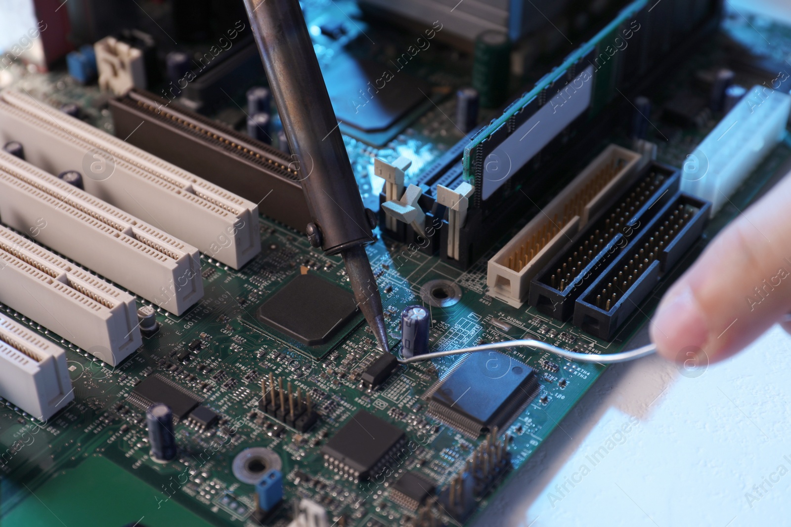 Photo of Technician repairing electronic circuit board with soldering iron at table, closeup