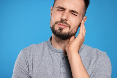 Young man suffering from ear pain on light blue background