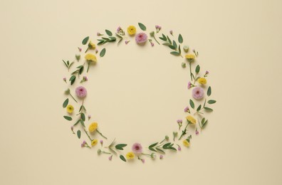Photo of Wreath made of beautiful flowers and green leaves on beige background, flat lay. Space for text