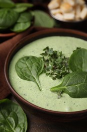 Photo of Delicious spinach cream soup with fresh leaves and microgreens in bowl on wooden table, closeup