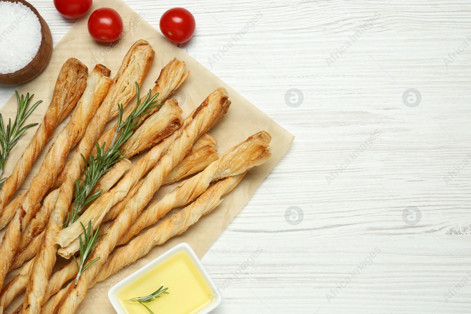 Photo of Delicious grissini, rosemary, salt, oil and tomatoes on white wooden table, flat lay. Space for text