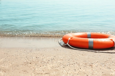 Photo of Orange life buoy on sand near sea. Emergency rescue equipment
