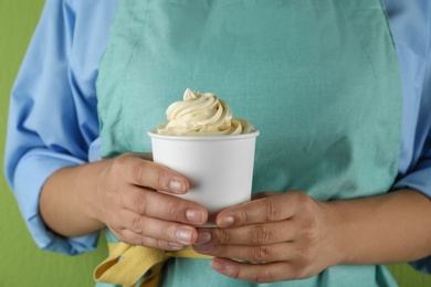 Woman holding cup with tasty frozen yogurt on green background, closeup