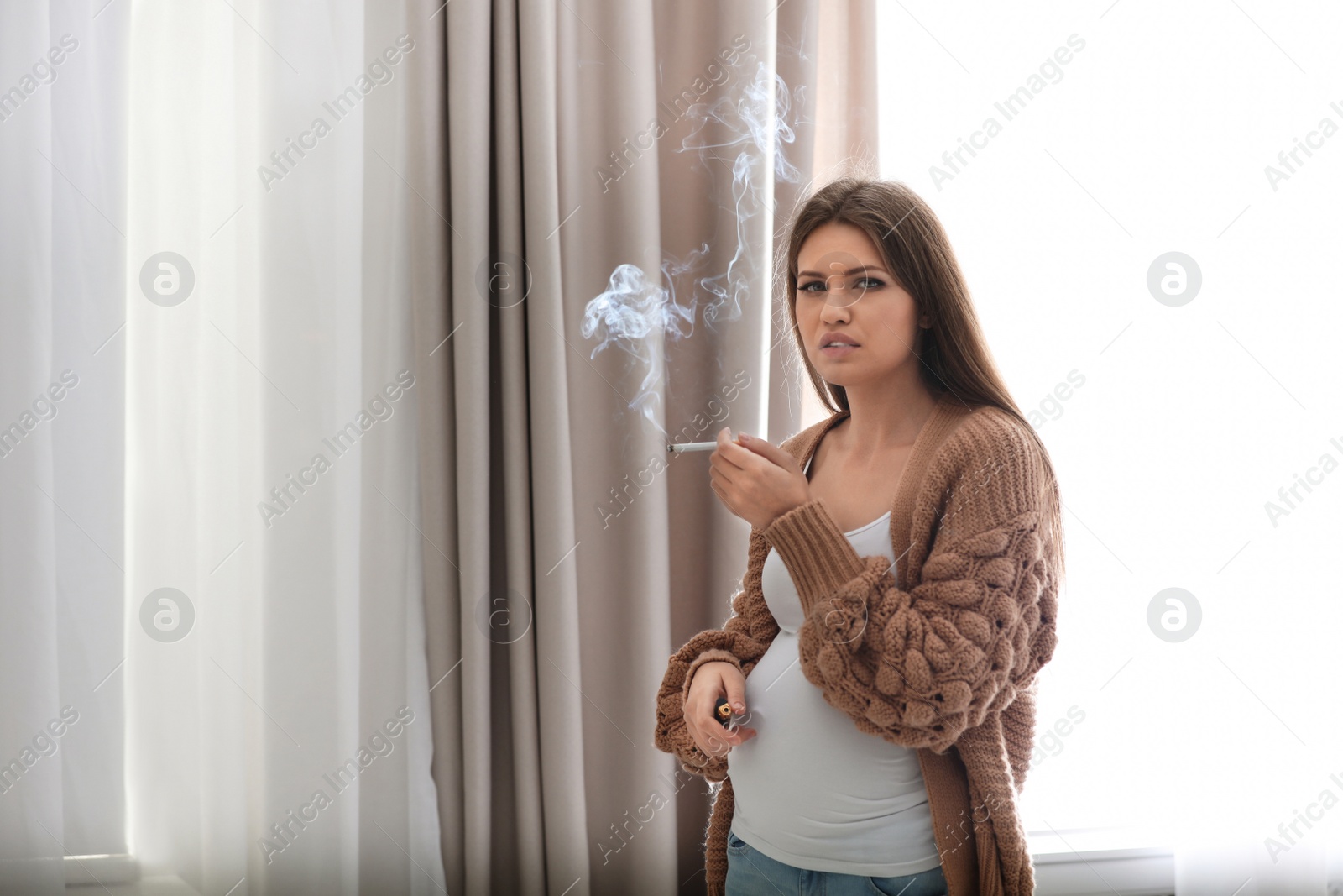 Photo of Young pregnant woman smoking cigarette at home. Harm to unborn baby