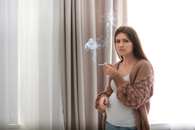 Photo of Young pregnant woman smoking cigarette at home. Harm to unborn baby