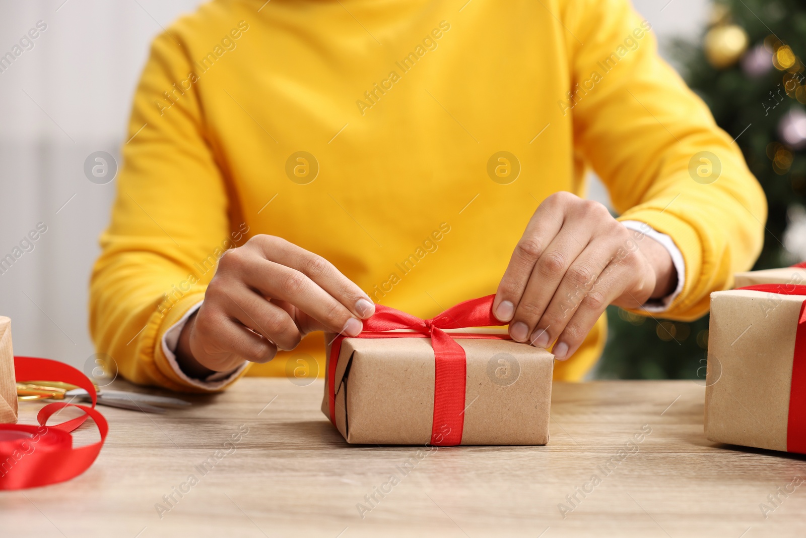 Photo of Man decorating Christmas gift box at wooden table indoors, closeup