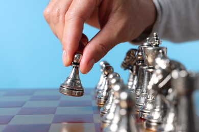 Man with game piece playing chess over checkerboard against light blue background, closeup