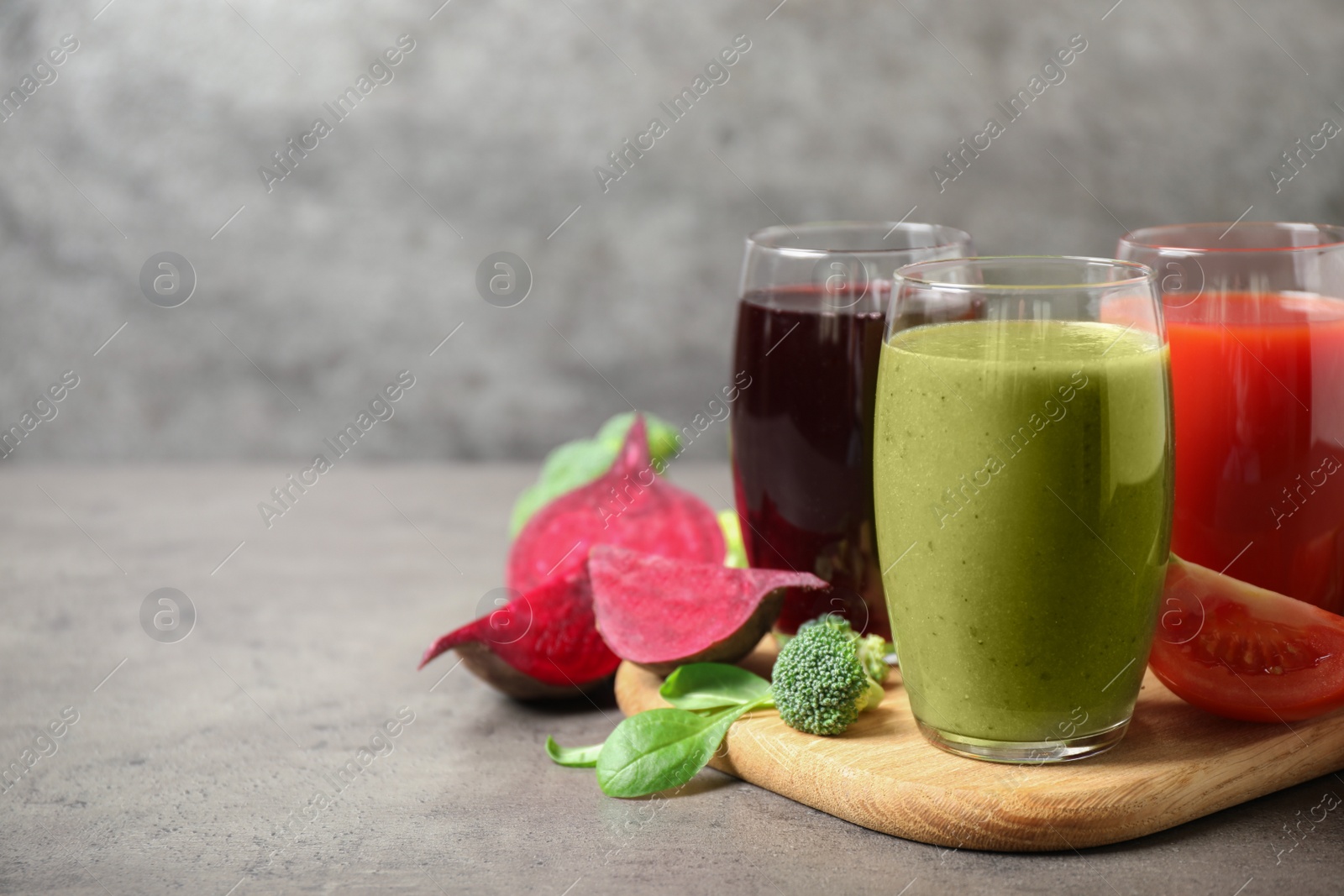Photo of Delicious vegetable juices and fresh ingredients on grey table. Space for text