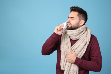 Man using nasal spray on light blue background, space for text