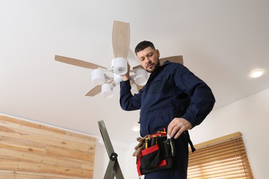 Photo of Electrician repairing ceiling fan with lamps indoors