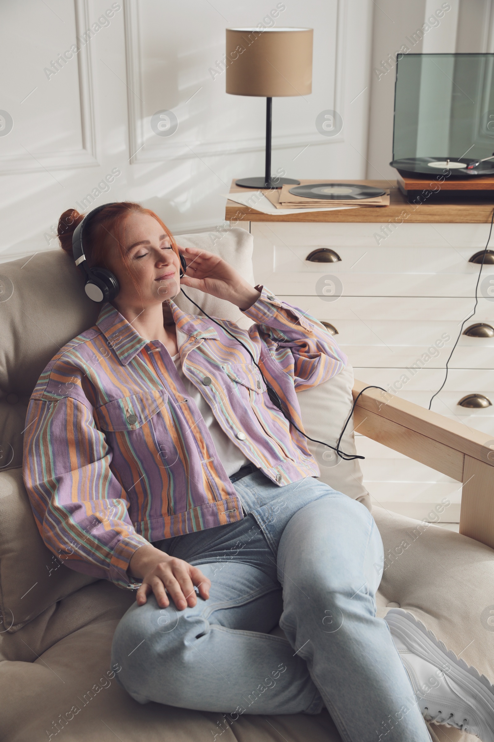 Photo of Young woman listening to music with turntable in living room