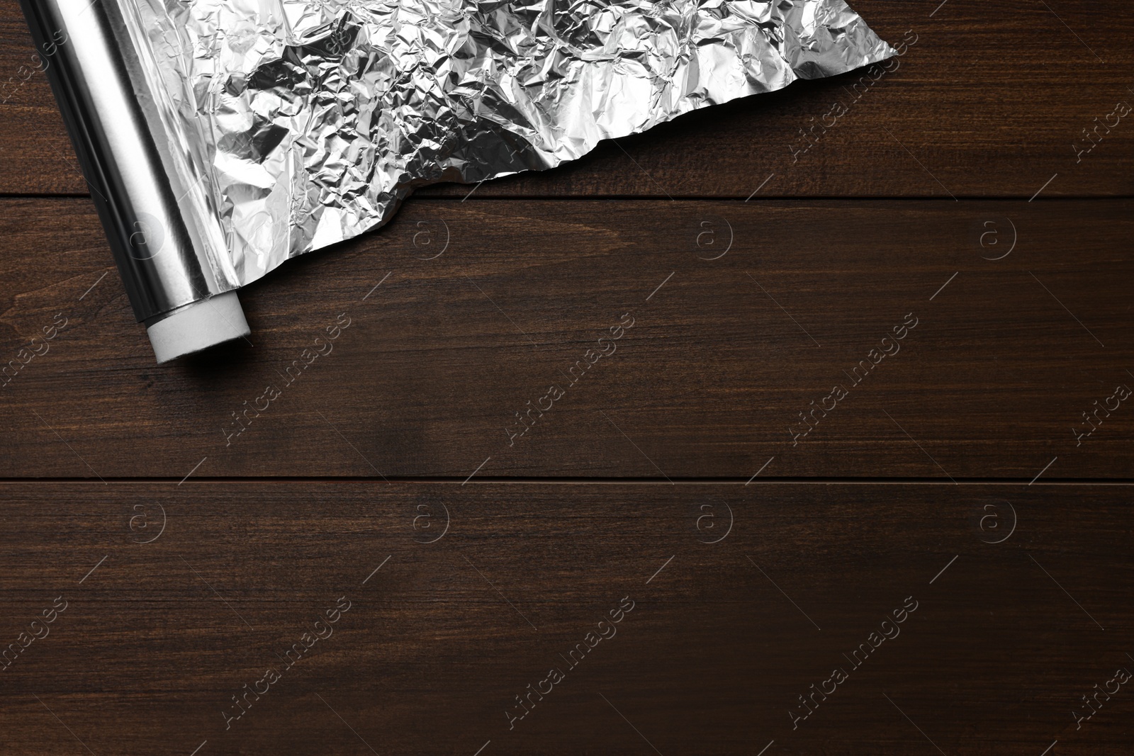 Photo of Roll of foil paper on wooden table, top view. Space for text